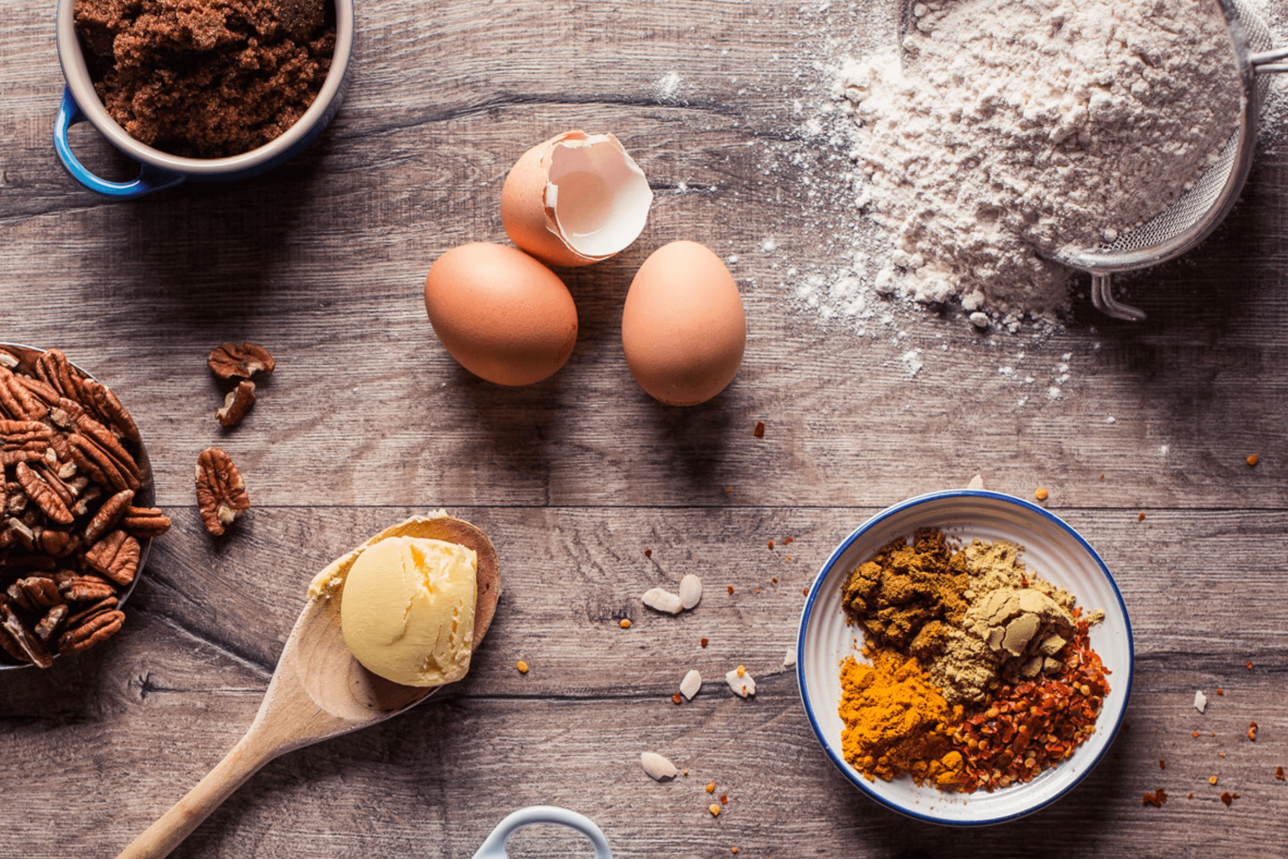 Baking ingredients: eggs, flour, butter, pecans and spices on a wooden table