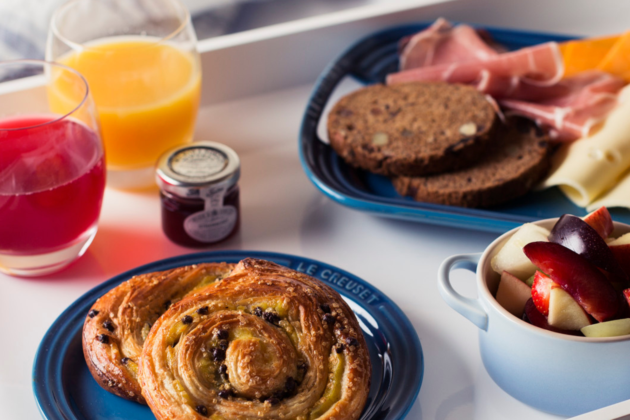 Breakfast table of pastries, rye bread, ham, cheese, fruit and juice